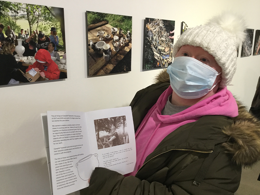 A maker stands with the brochure open in front of pictures of the potters celebrating